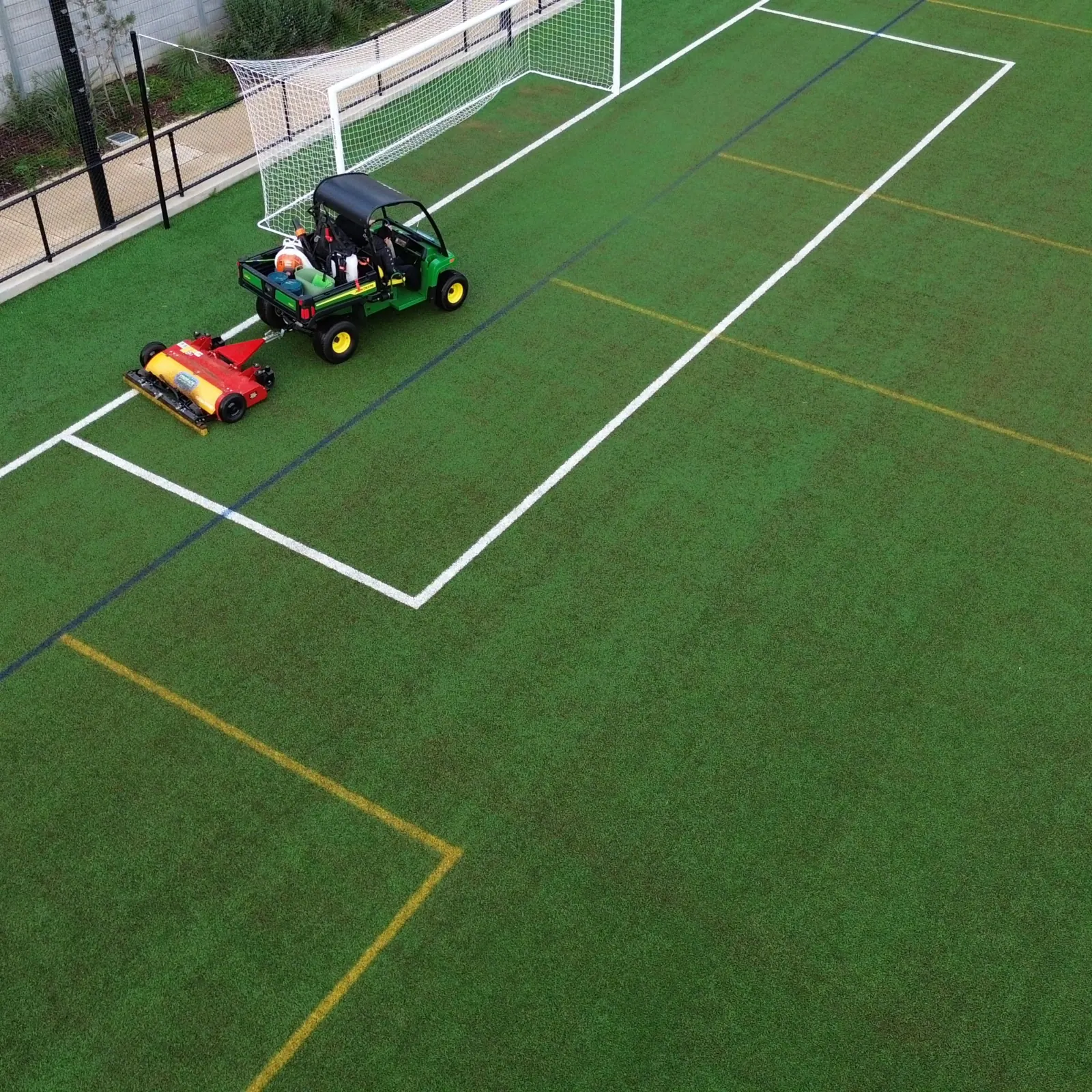 Utility vehicle towing a groomer across a synthetic football pitch beside the goal