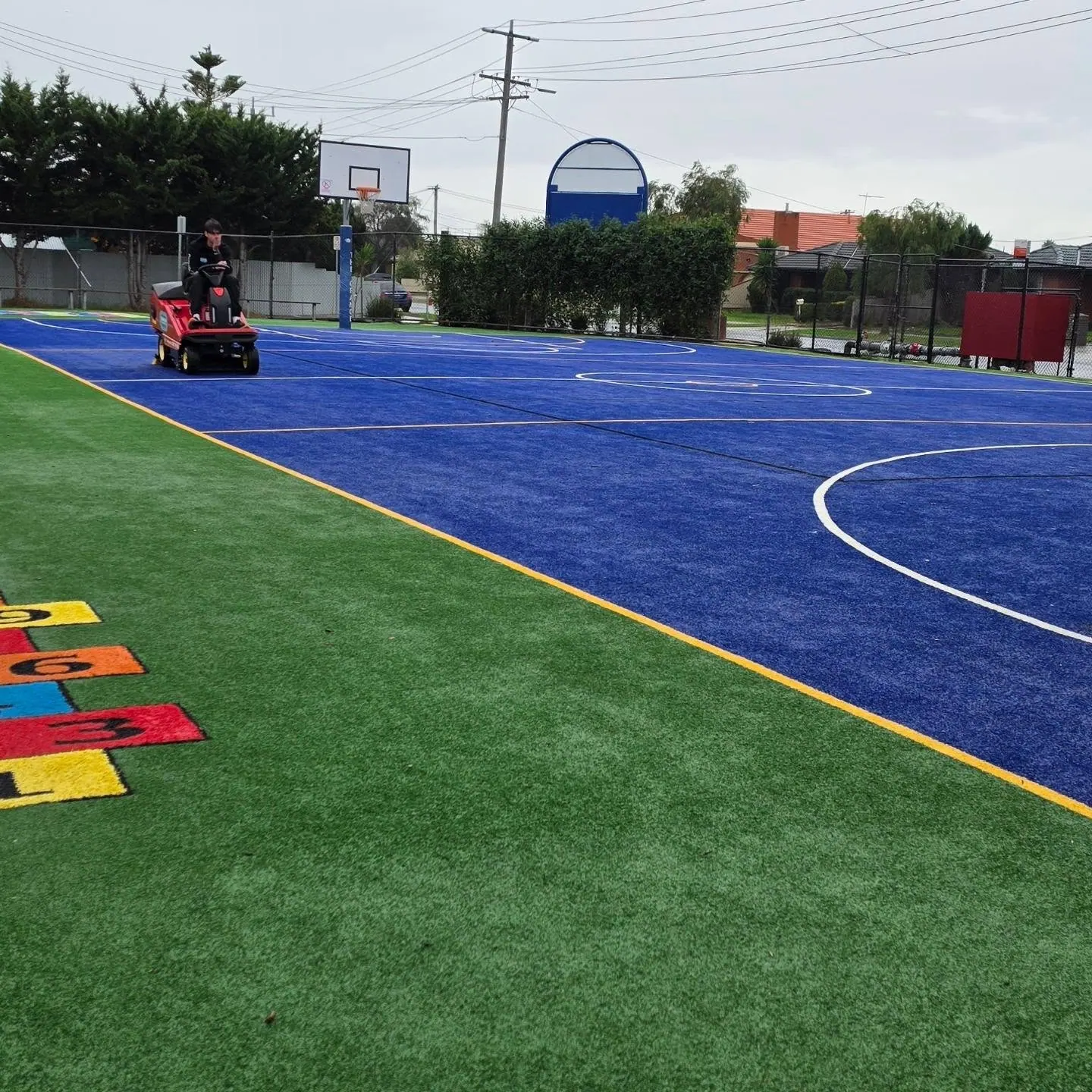Blue synthetic court alongside a green play area with painted hopscotch markings